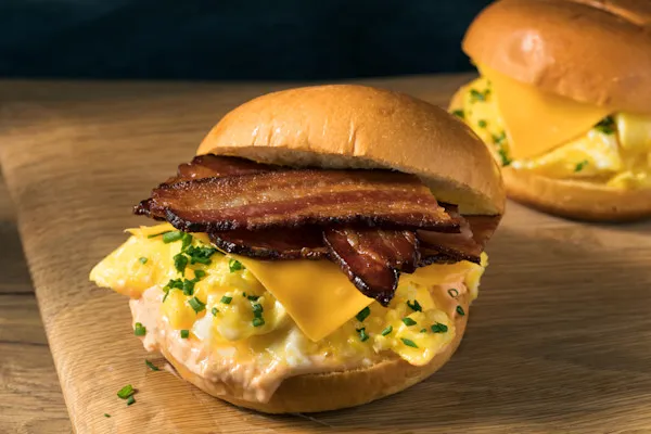 Delicious bacon and egg sandwich, thick-cut crispy bacon, fluffy scrambled eggs, melted pepper jack cheese, and fresh organic spring mix, all served on a freshly baked brioche bun.